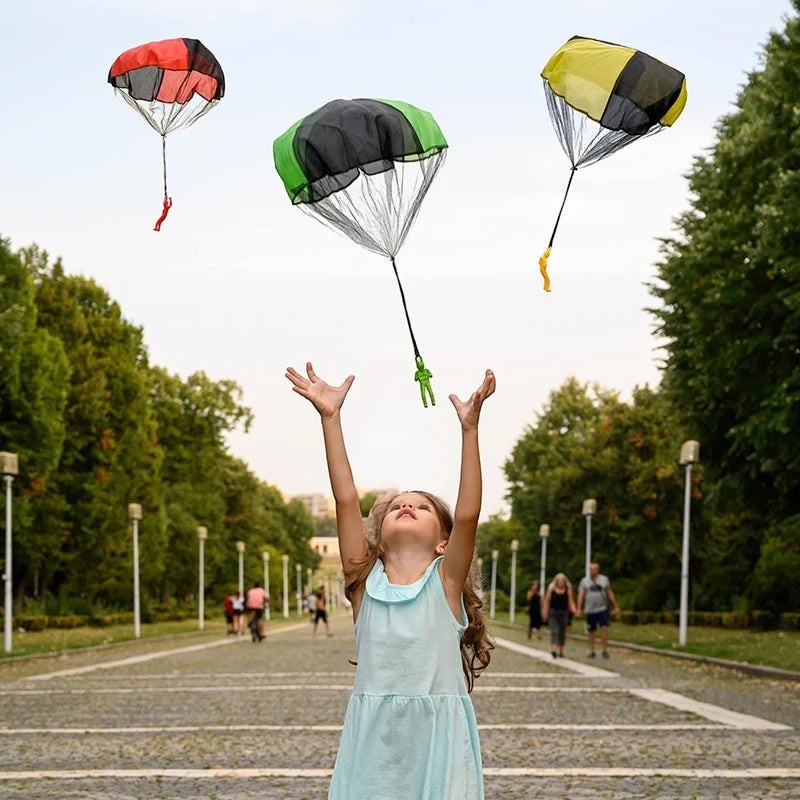 Petit Éveil Montessori : enfant lançant des parachutes jouets multicolores (rouge, vert, jaune) dans un parc.