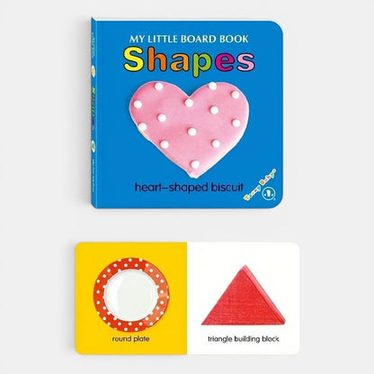 Petit Éveil Montessori : livre cartonné "Shapes" avec biscuit en forme de cœur rose à pois blancs et pages intérieures montrant une assiette ronde et un bloc de construction triangulaire rouge.