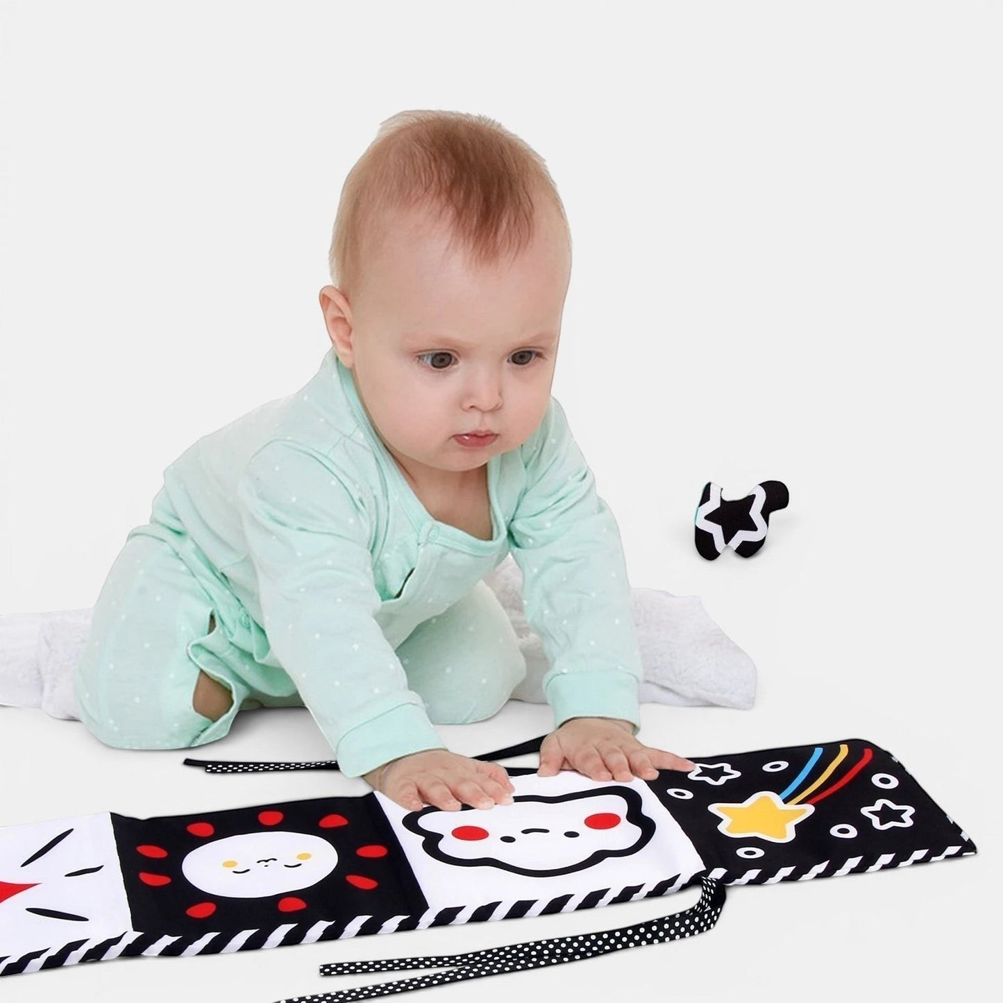Livre sensoriel en tissu noir et blanc Petit Éveil Montessori avec des motifs de soleil, nuage et étoile. Bébé explore le livre.