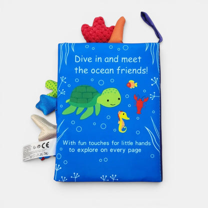 Livre en tissu Petit Éveil Montessori bleu avec une tortue, un hippocampe, un poisson et un homard. Touches amusantes pour les petites mains.