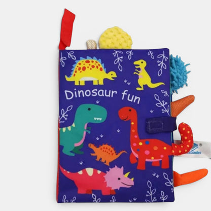 Livre en tissu Petit Éveil Montessori bleu avec des dinosaures colorés et des textures variées pour bébé.