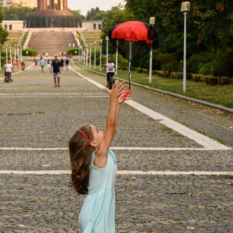 Petit Éveil Montessori : petite fille jouant avec un parachute rouge et noir en extérieur, favorisant la coordination et le jeu collectif.